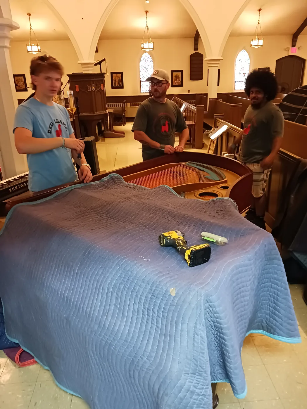 Red Llama movers preparing a grand piano at an event venue.