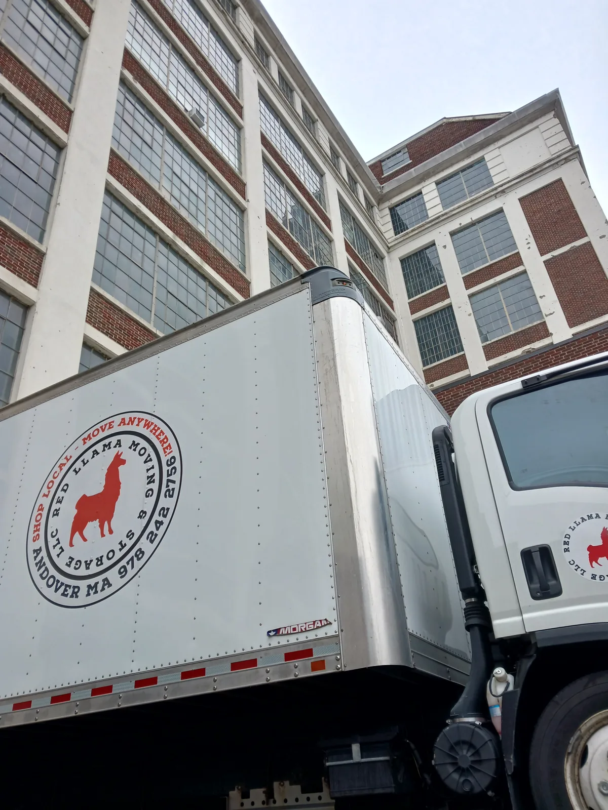 Red Llama moving truck beside a commercial building.
