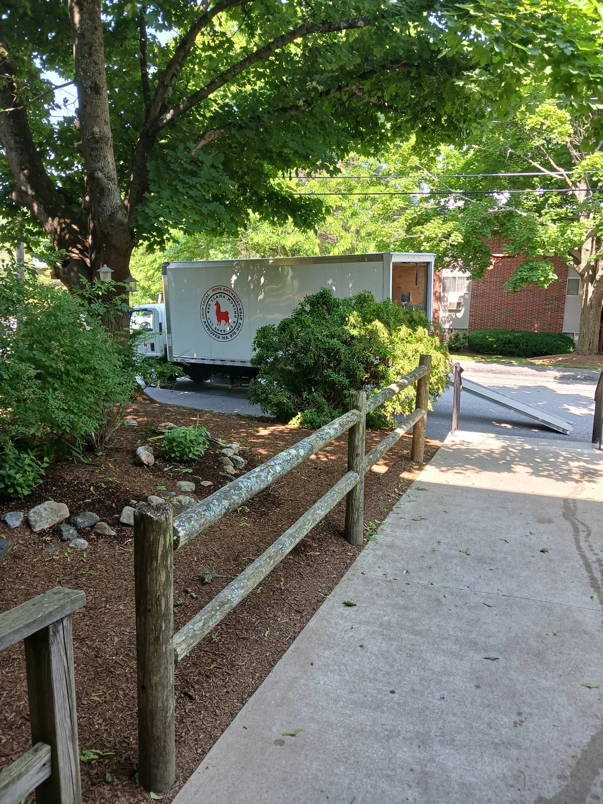 Red Llama moving truck with its ramp open at a wooded residential property.